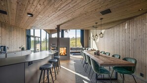 A modern kitchen with a central island, bar stools, and a dining area with green chairs. - Stunning view in holiday home (Gol)