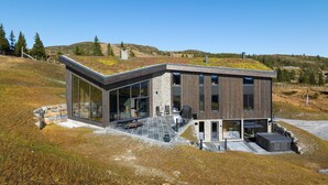 A modern house with large glass windows, a stone facade, and a sloped roof covered with vegetation. - Stunning view in holiday home (Gol)