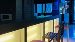 Uma área de bar moderna com balcão, banquetas e vista para a cidade através de grandes janelas.