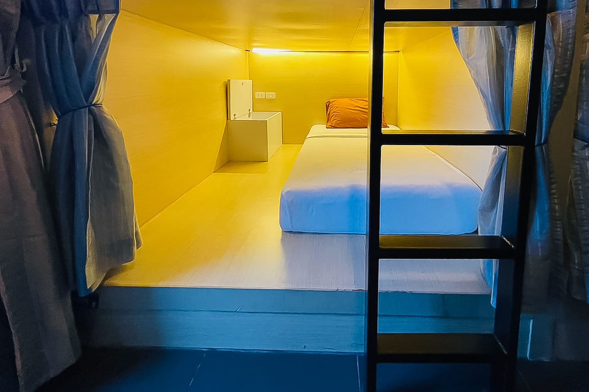 A compact room with a bunk bed, a small bedside table, and a wall-mounted light fixture.