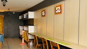 Uma área de refeições moderna com uma mesa comprida e cadeiras de madeira, um ventilador e uma parede com duas imagens emolduradas.