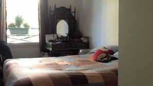 Une chambre à coucher comprenant un lit, une commode, un miroir et une fenêtre donnant sur un paysage verdoyant.