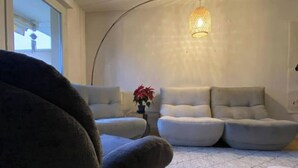 Un salon chaleureux avec un grand fauteuil, deux canapés, une petite table ornée d’une plante et un luminaire suspendu.