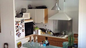 Une cuisine compacte équipée d’un four à micro-ondes, d’un réfrigérateur et d’une cuisinière. On y trouve une table en verre et une chaise.