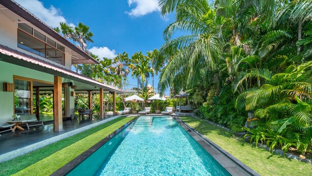Une piscine à l’eau d’un bleu cristallin, entourée d’une végétation luxuriante et de palmiers.