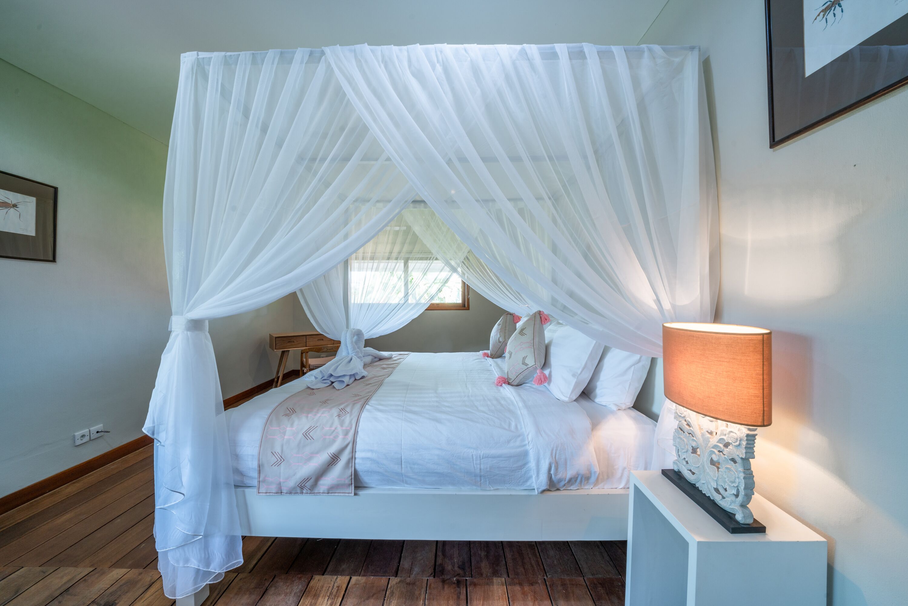 Un dormitorio con cama a dosel, una mesita de noche con lámpara y un cuadro enmarcado en la pared.