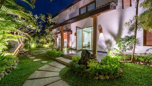 Un jardin bien entretenu, avec un chemin de pierres menant à une maison dotée de grandes portes vitrées.