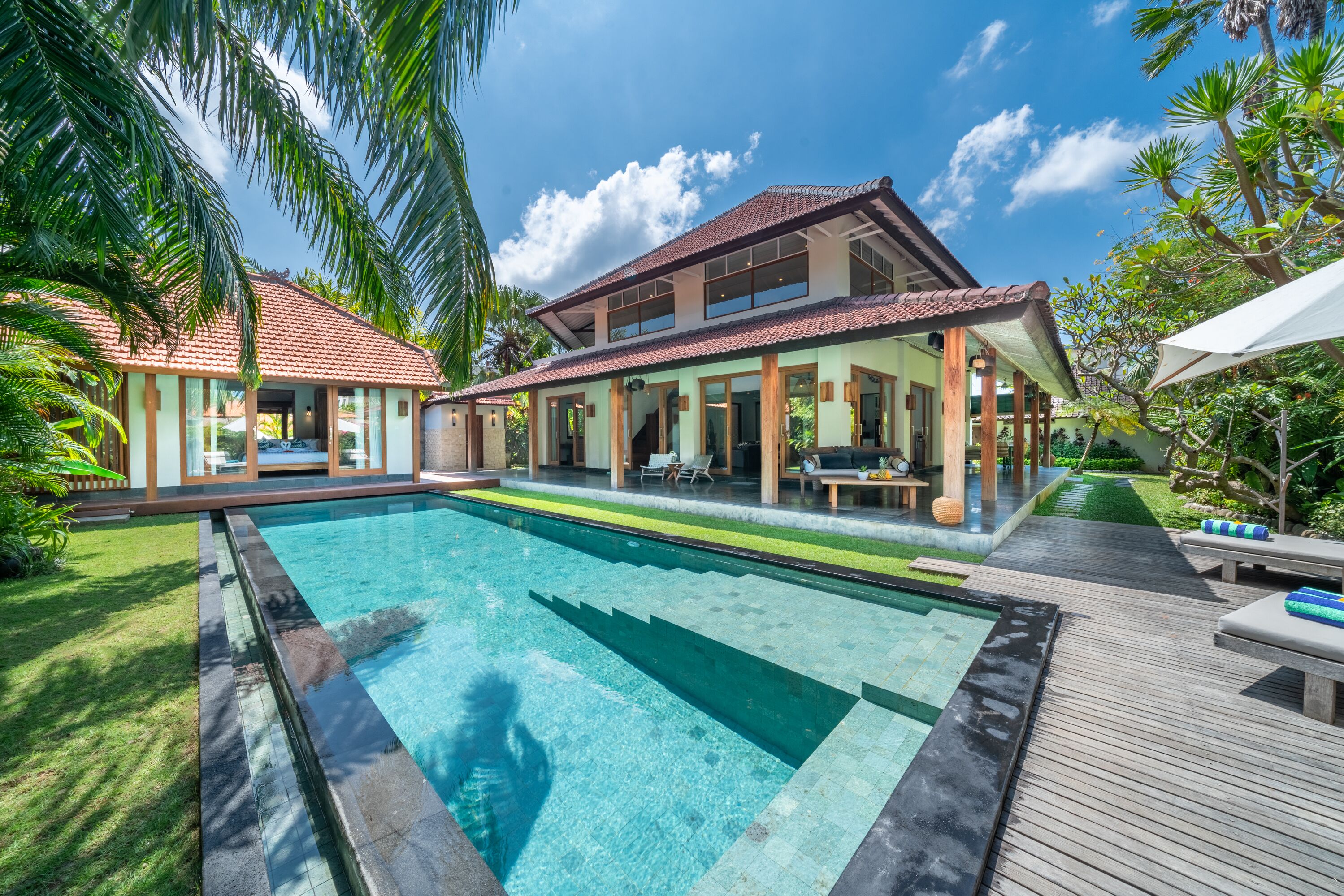 A modern house with a swimming pool, covered patio, and lush greenery.