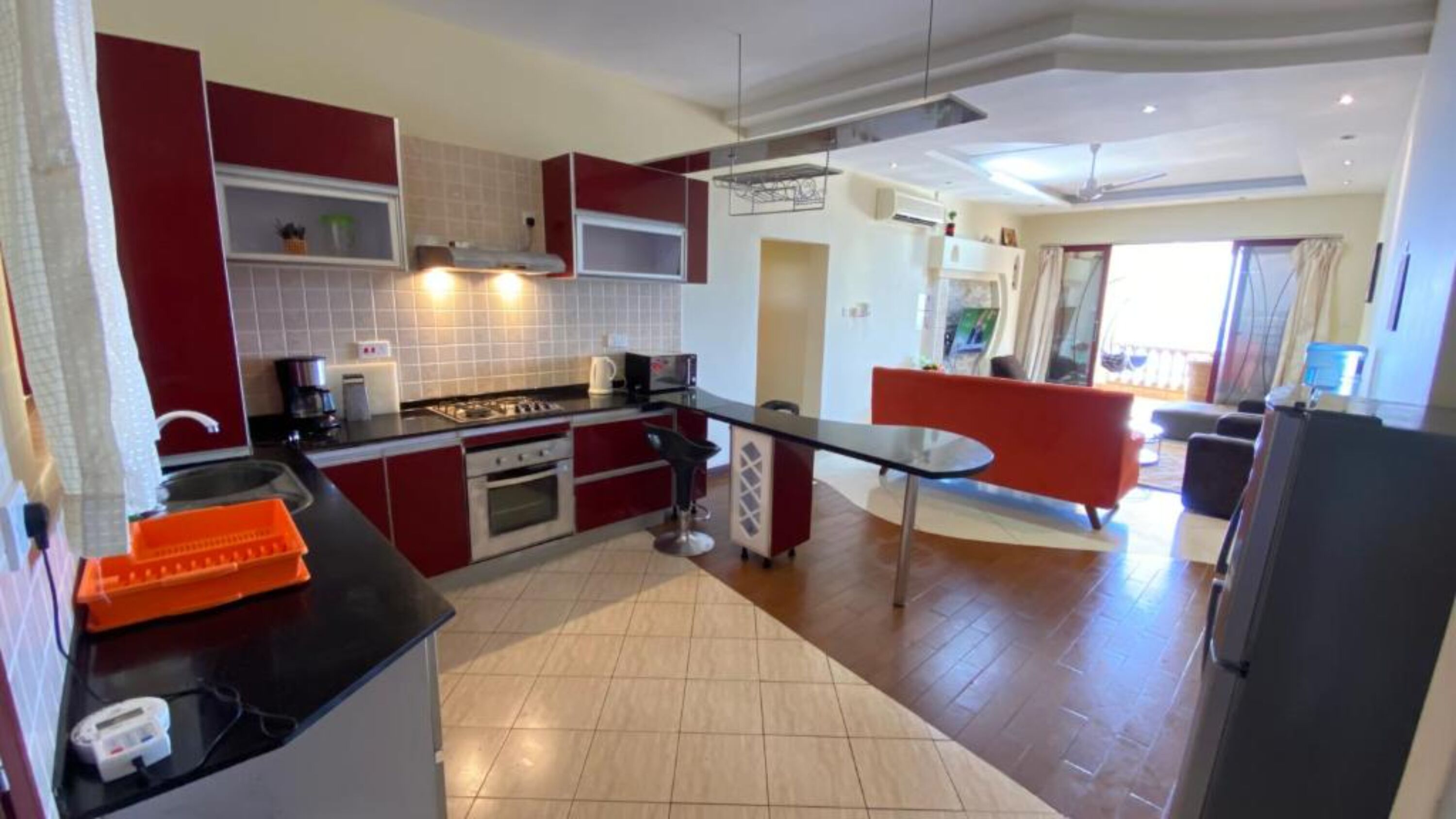 A modern kitchen with red cabinets, a black countertop, and a dining area with a red bench.