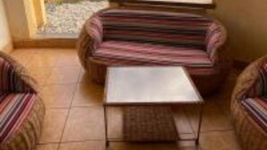 Patio con divani a righe e un tavolino, vista su piscina e vegetazione.