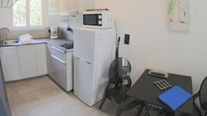 Una cucina compatta con mobili bianchi, un forno a microonde e un frigorifero. C'è un tavolo da pranzo con una sedia e una cartella blu sopra.