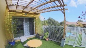 Un portico riparato con tavolo e sedie, un piccolo giardino e un recinto bianco.