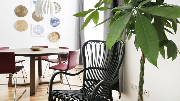 A dining area with a round table, red chairs, and a black chair with a woven backrest.