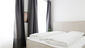 A neatly made bed with white bedding, a quilted headboard, and a small potted plant on the nightstand.