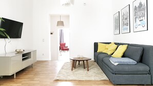 Ein modernes Wohnzimmer mit einem grauen Sofa, einem kleinen runden Tisch und einem Flachbildfernseher an einer weißen Wand.