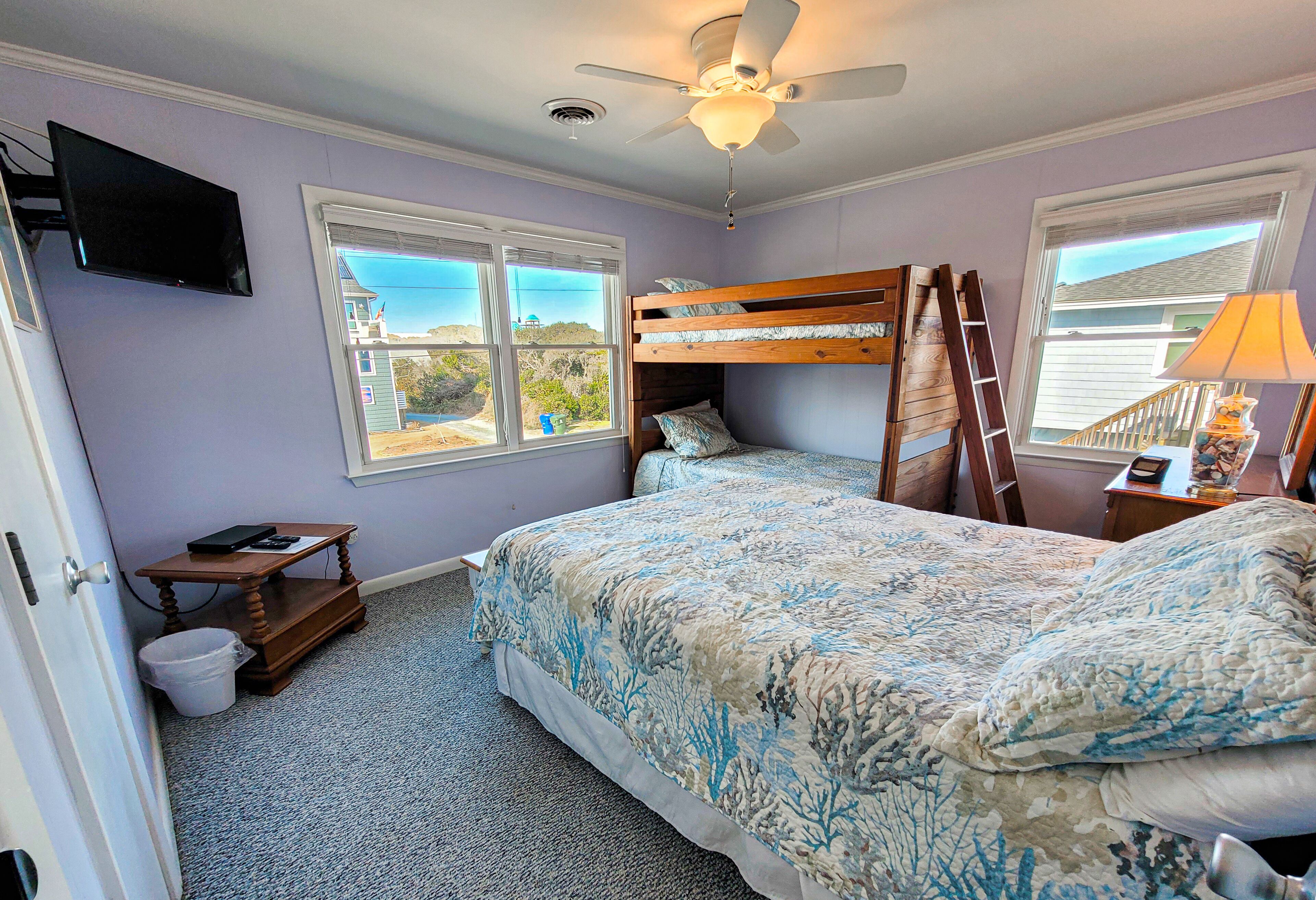 A bedroom with a bunk bed, a ceiling fan, a TV, and a view of the outside.