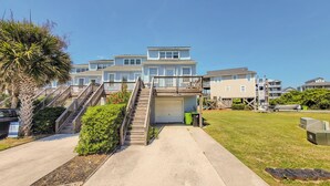 A beachfront residential building with multiple levels, a covered garage, and a staircase leading to the upper floors.