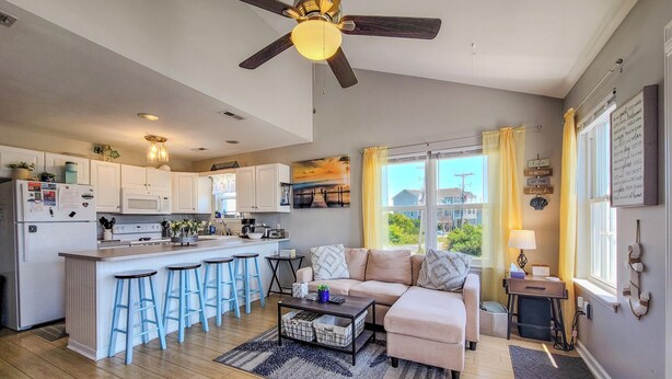 A spacious kitchen with a central island, a dining area with bar stools, a sofa, and a view of the outdoors.