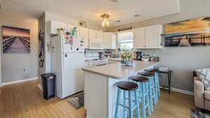 A modern kitchen with white cabinets, a central island with bar stools, a refrigerator, and a microwave.