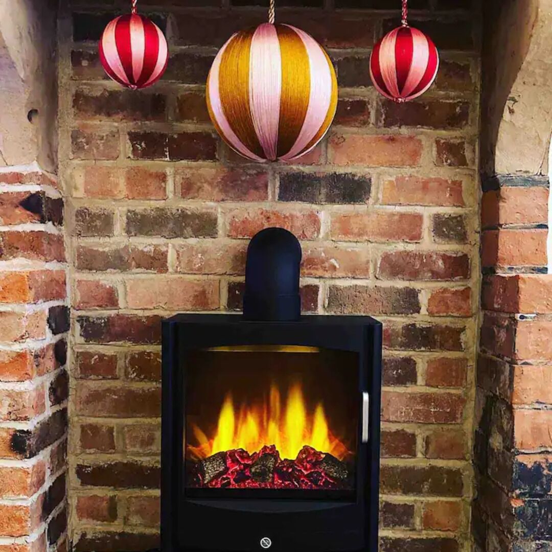 A fireplace with a visible fire, brick walls, and three striped ornaments hanging above it.
