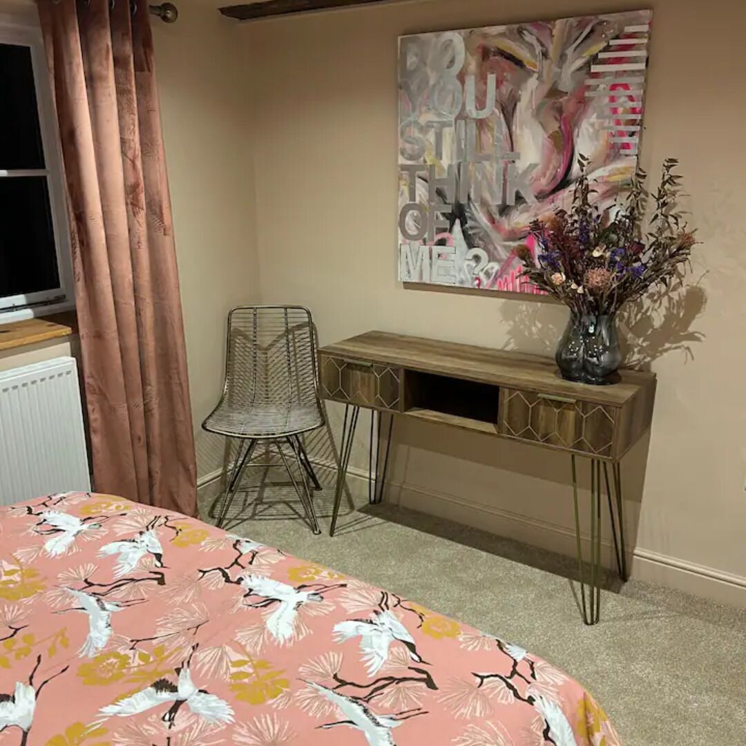 Ein Schlafzimmer mit Bett, Schreibtisch, Stuhl, einem Fenster mit Vorhängen und Wandkunst in abstrakter Gestaltung.