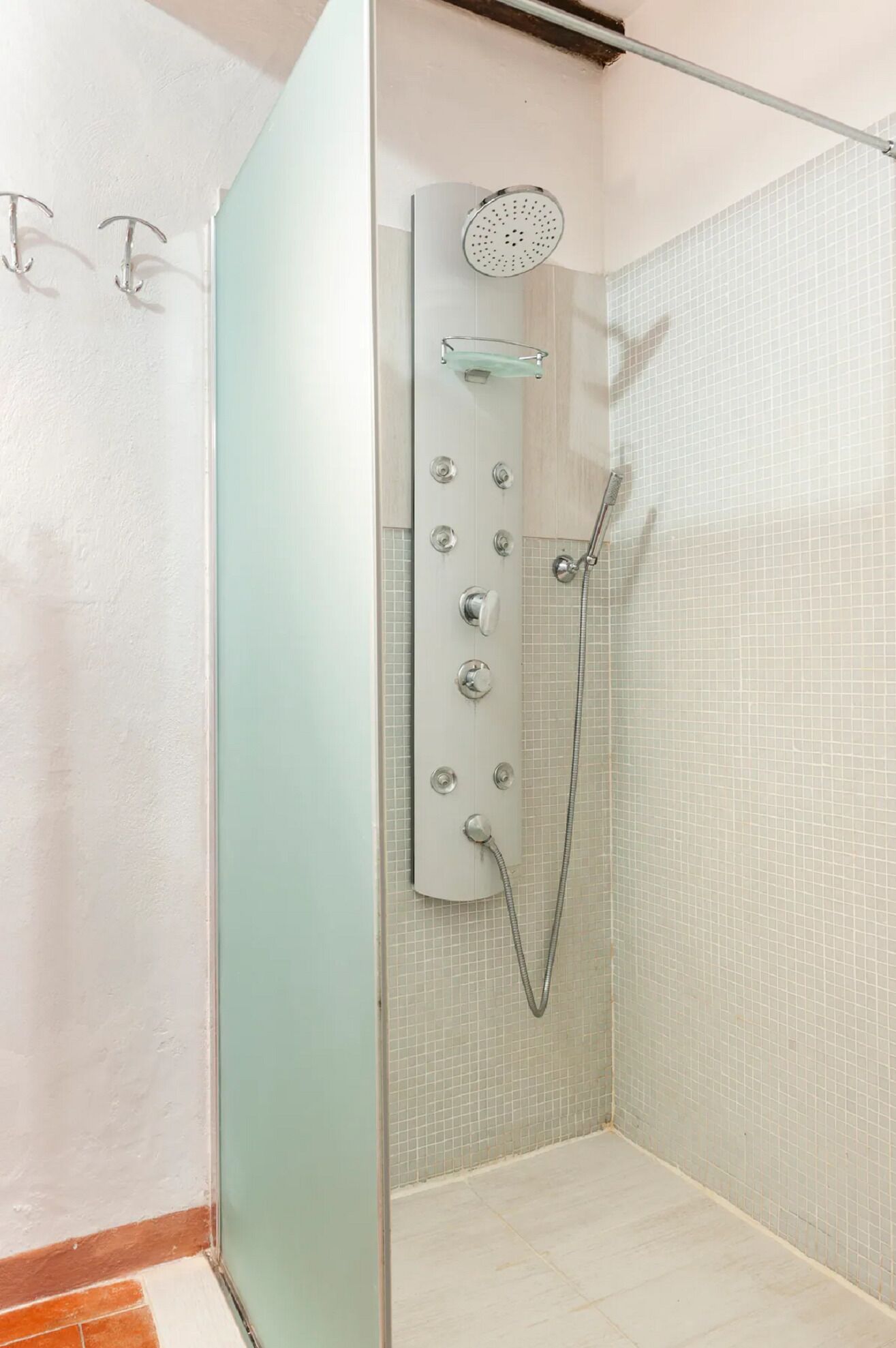 Eine begehbare Dusche mit Glaswänden, einer Handbrause und einem fest montierten Bedienfeld.