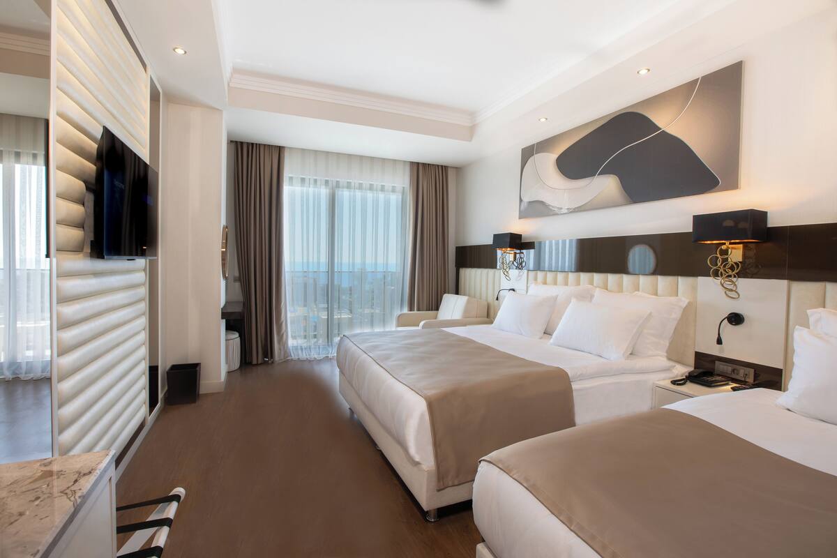 A hotel room with two beds, a TV, a large window with curtains, and a wall-mounted artwork.
