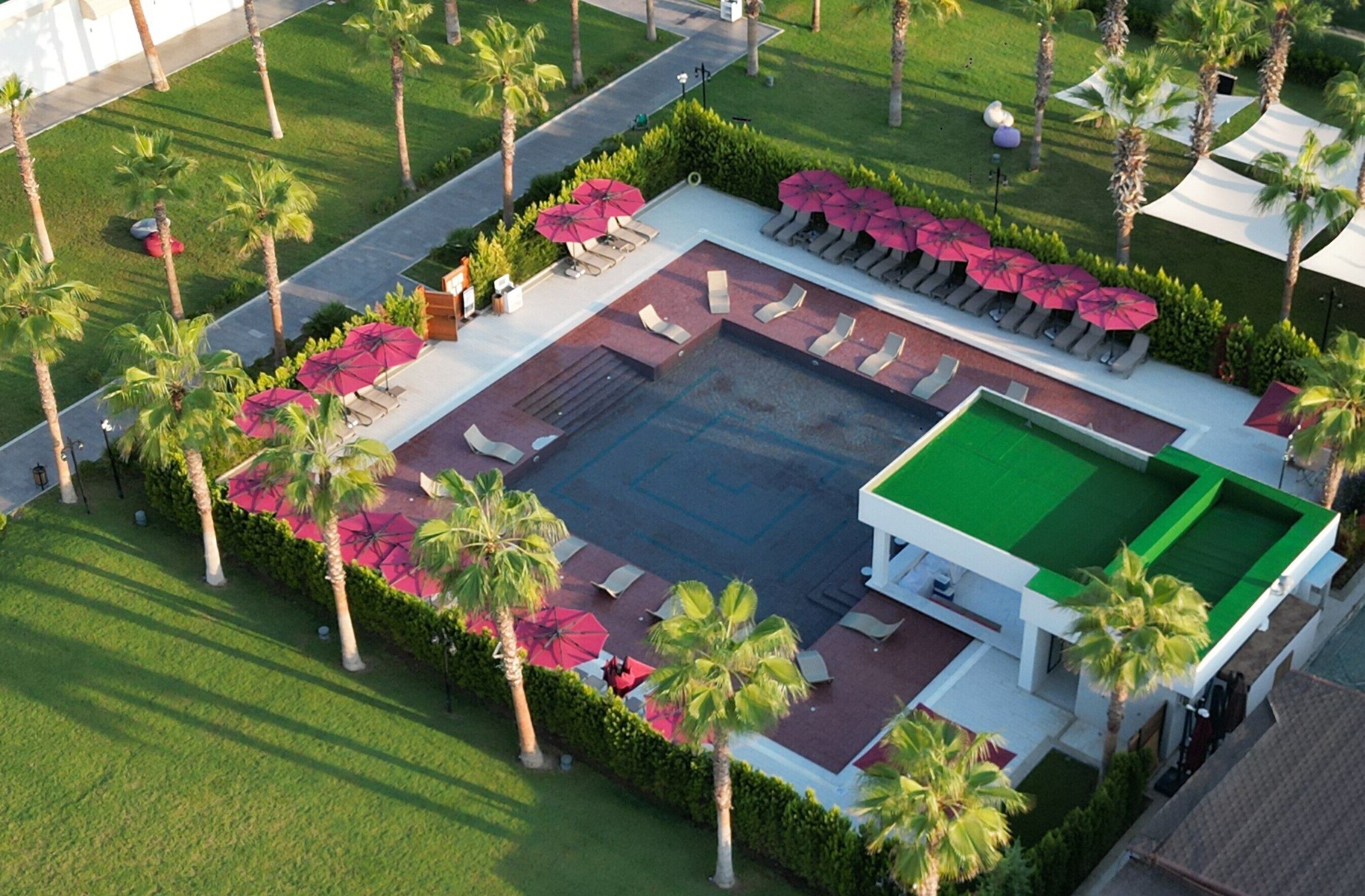 Vista aerea di un resort con piscina, lettini e palme.