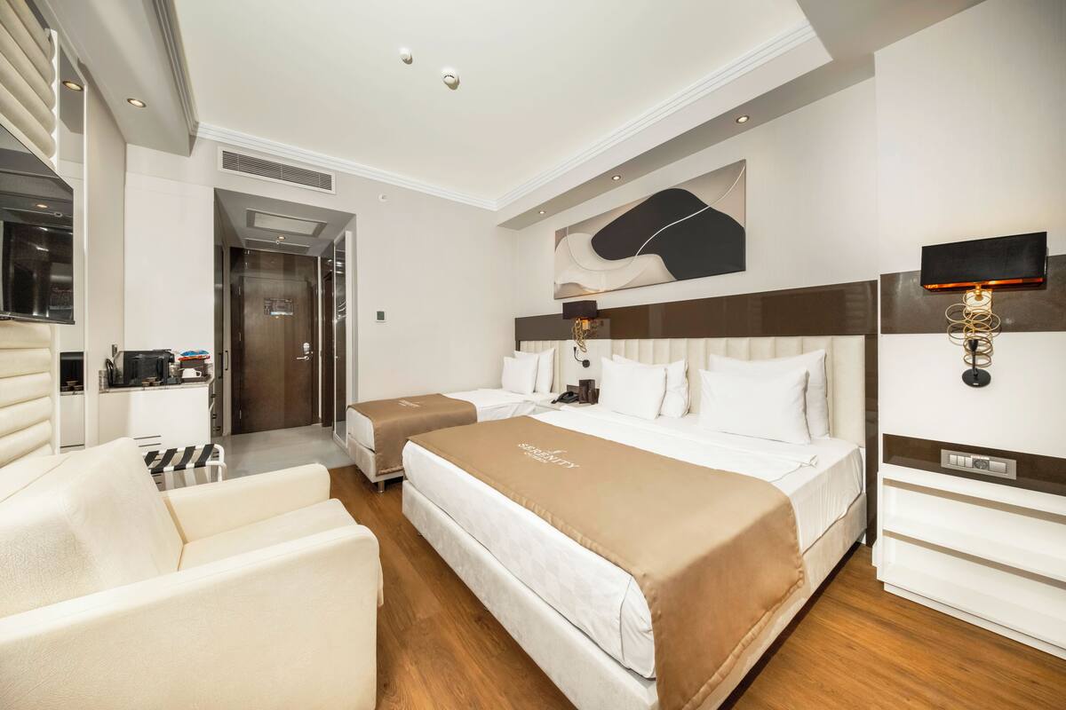 A hotel room with two beds, a sofa, a desk, and a kitchenette.