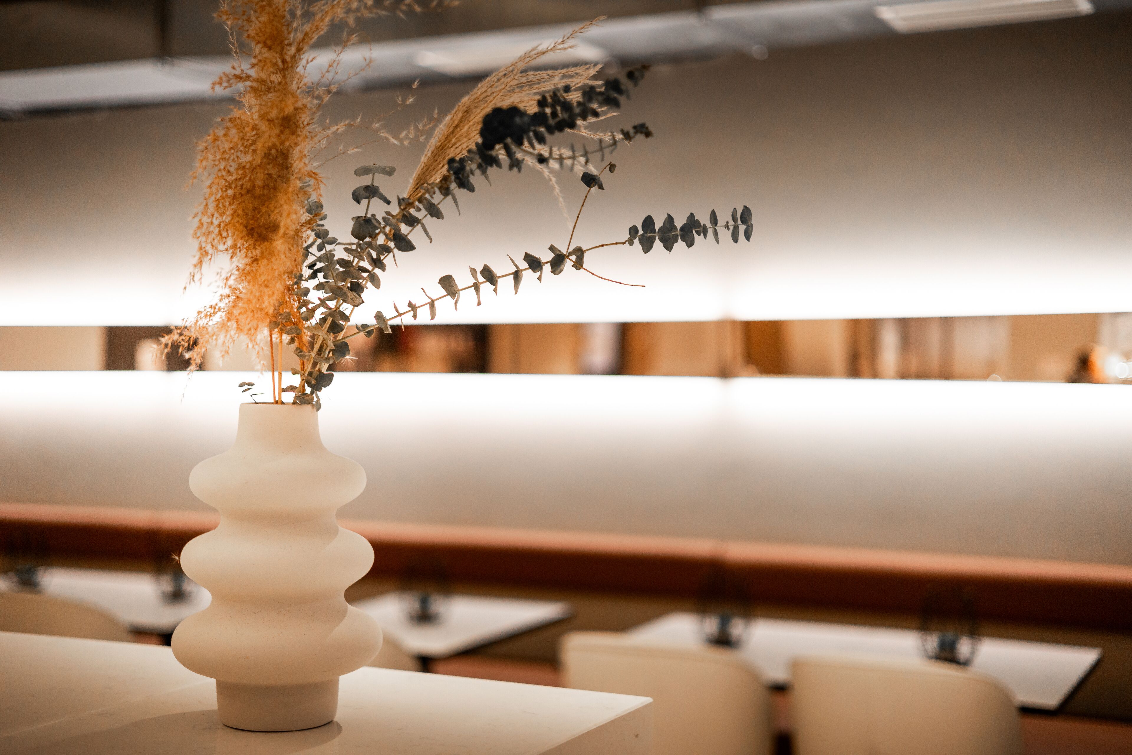 Eine weiße Vase mit Trockenpflanzen auf einem Tisch in einem Restaurant.