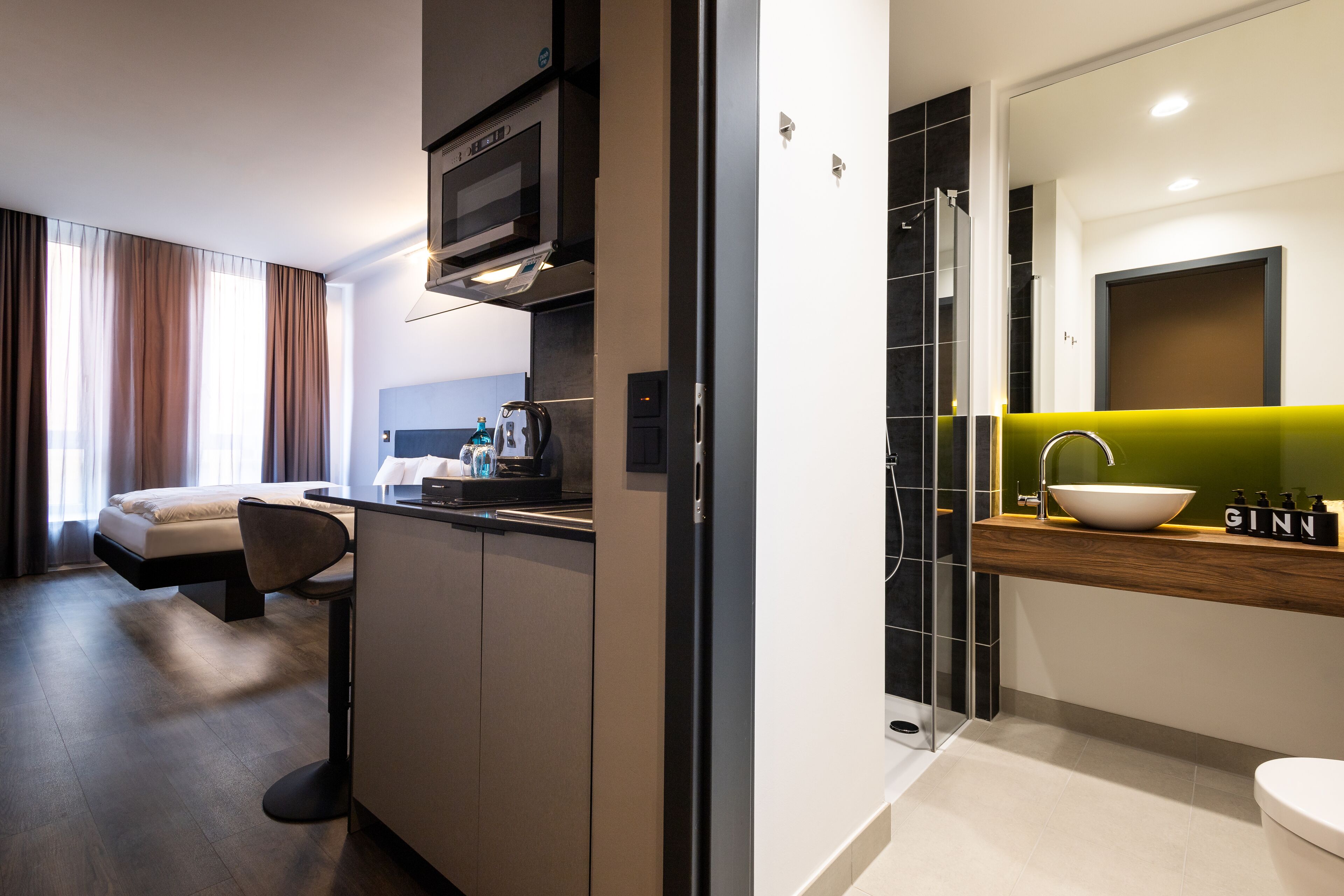 Une chambre d’hôtel moderne dotée d’une kitchenette, d’un grand lit, d’un coin salon et d’une salle de bain avec un grand miroir et un lavabo.