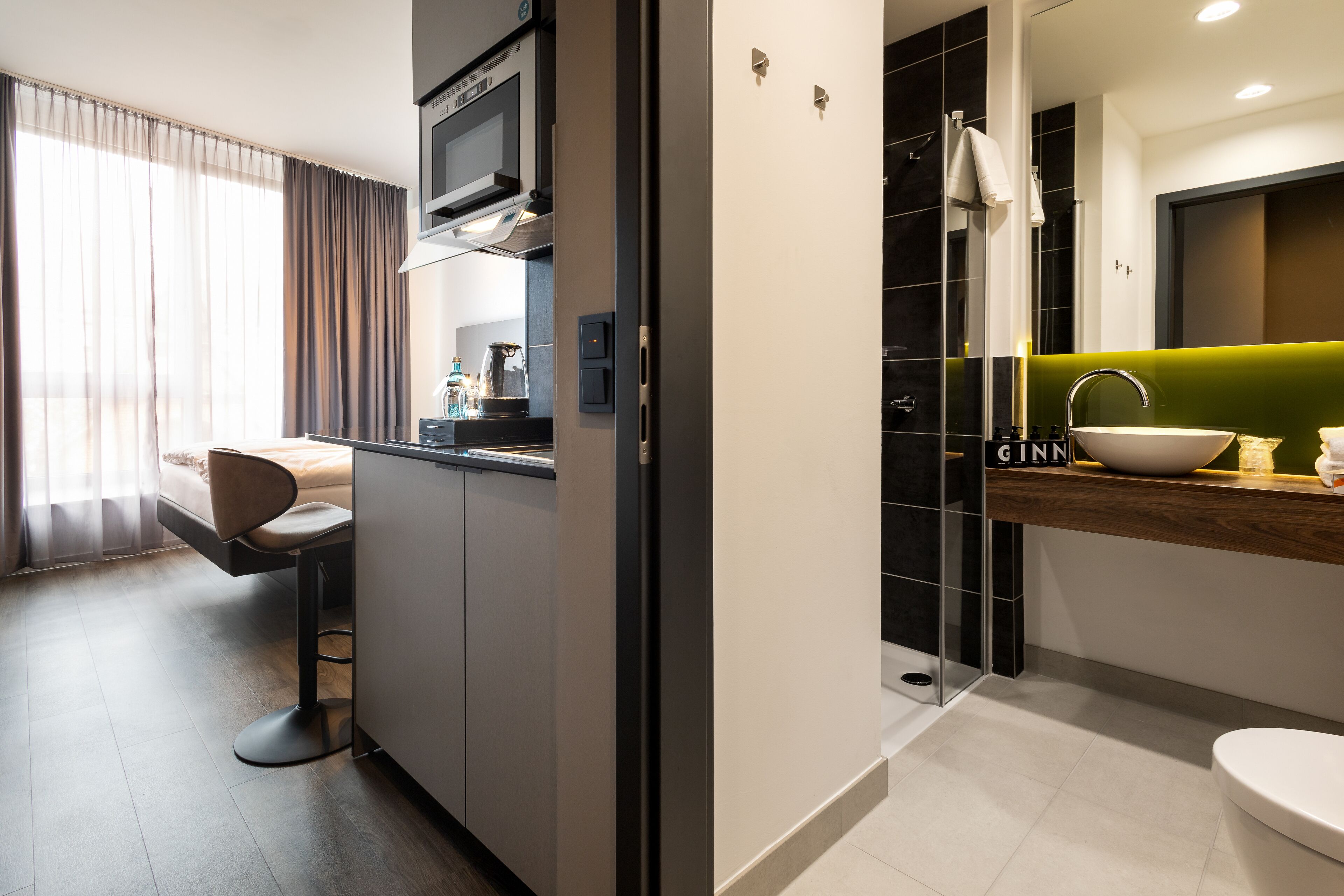 A modern kitchen with a built-in oven, a dining area with a chair, and a bathroom with a sink and toilet.