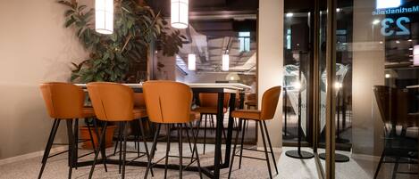 A modern dining area with a round table, orange chairs, and pendant lighting.