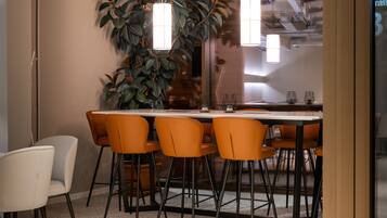 A modern dining area with a rectangular table, six orange chairs, and two pendant lights.