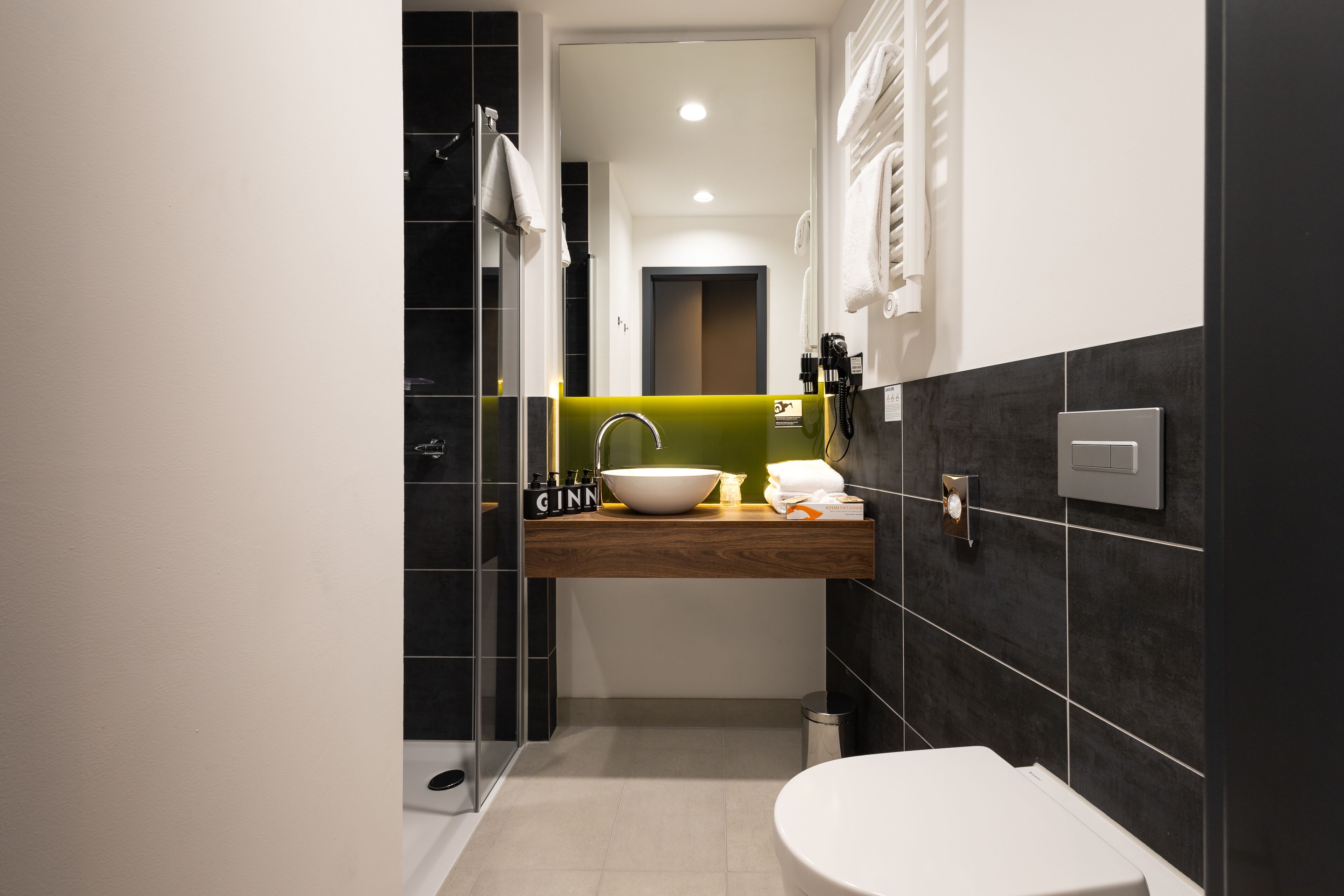 A modern bathroom with a white toilet, a sink with a wooden countertop, a mirror, and a shower area.