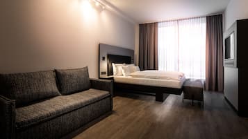 Une chambre d’hôtel moderne avec un grand lit, un canapé, une télévision et une grande fenêtre avec des rideaux.