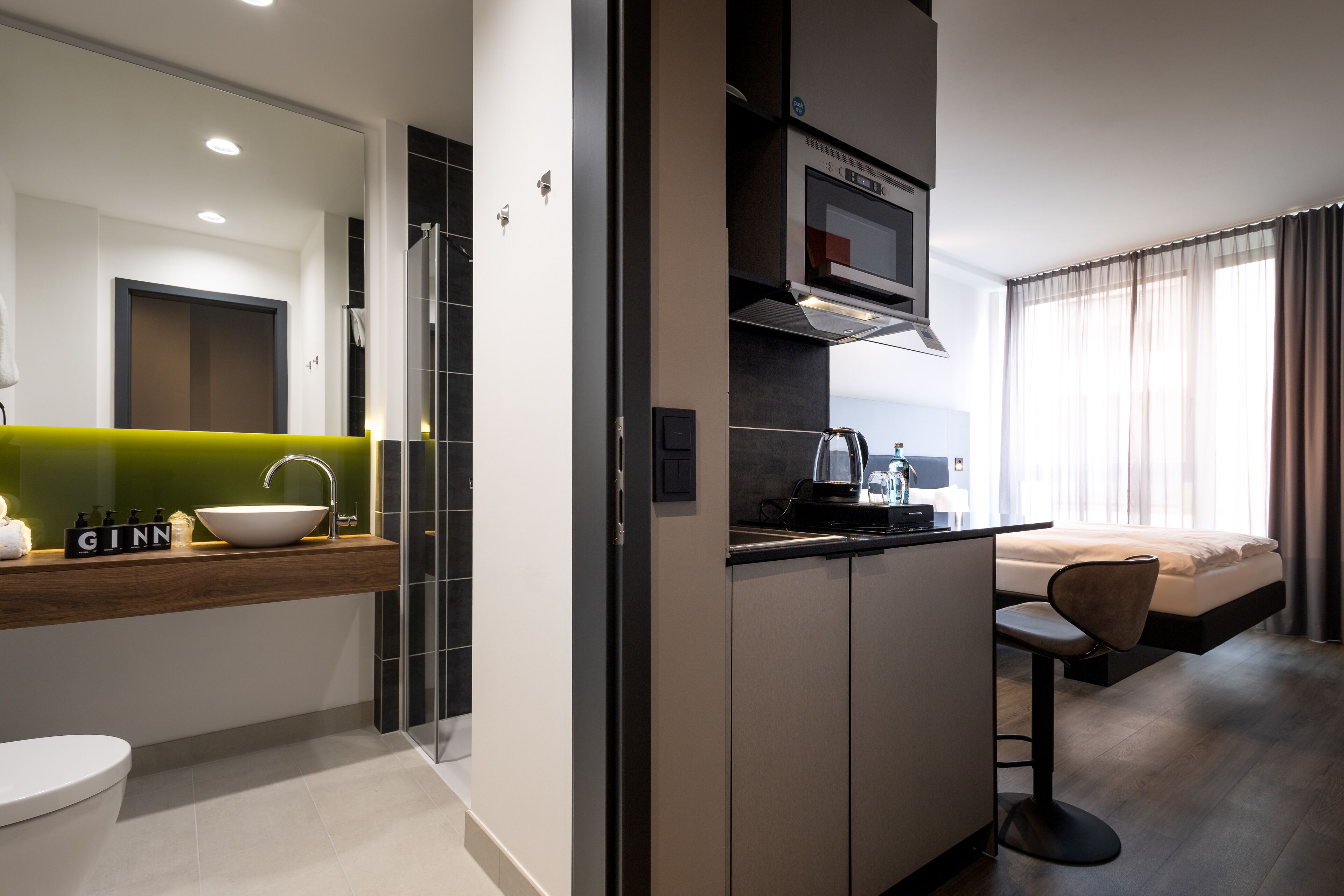 Ein modernes Hotelzimmer mit Küchenzeile, einem großen Spiegel, einer Toilette und einem Bett.