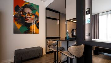 Une chambre d’hôtel moderne avec un coin bar, un banc et un grand tableau abstrait accroché au mur.
