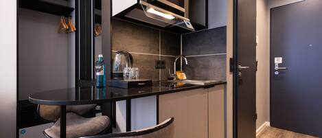 Una cocina moderna con encimera negra, armarios grises y horno empotrado. Hay una mesa redonda con sillas y una percha con perchas de madera.