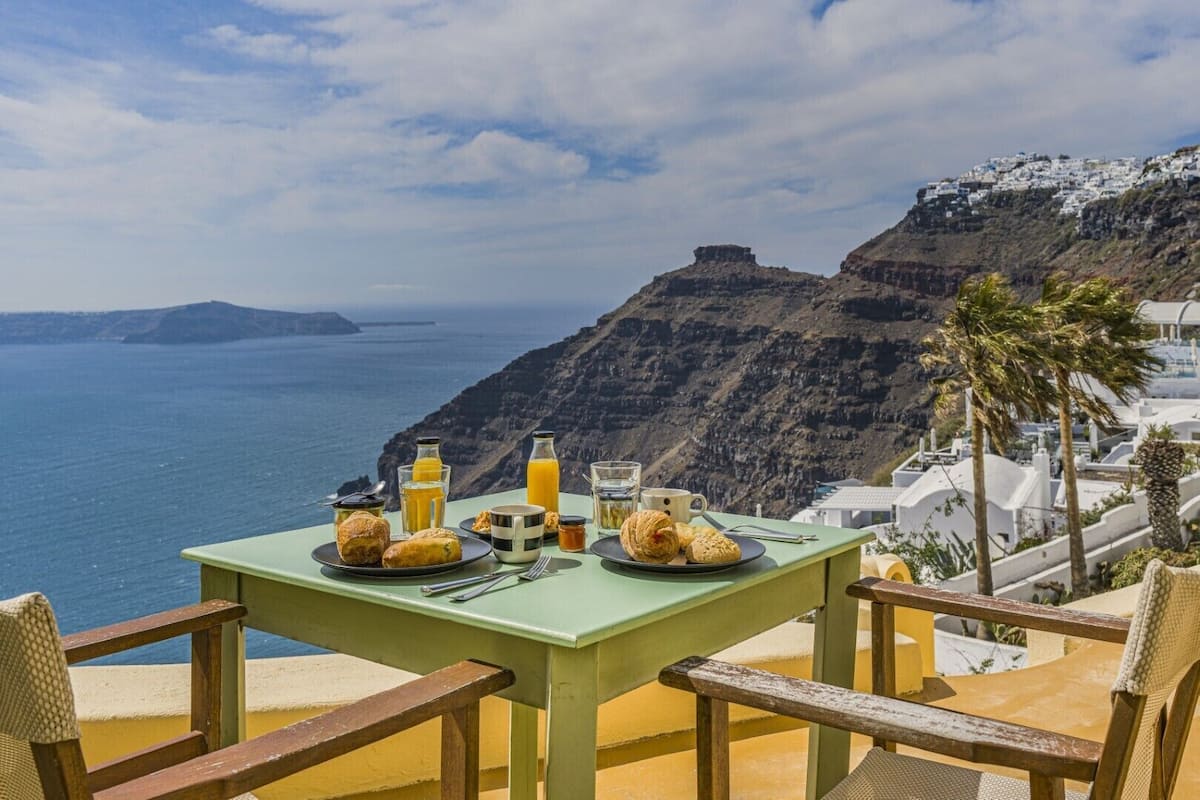 A table set with breakfast items overlooking a coastal landscape with white buildings and cliffs.