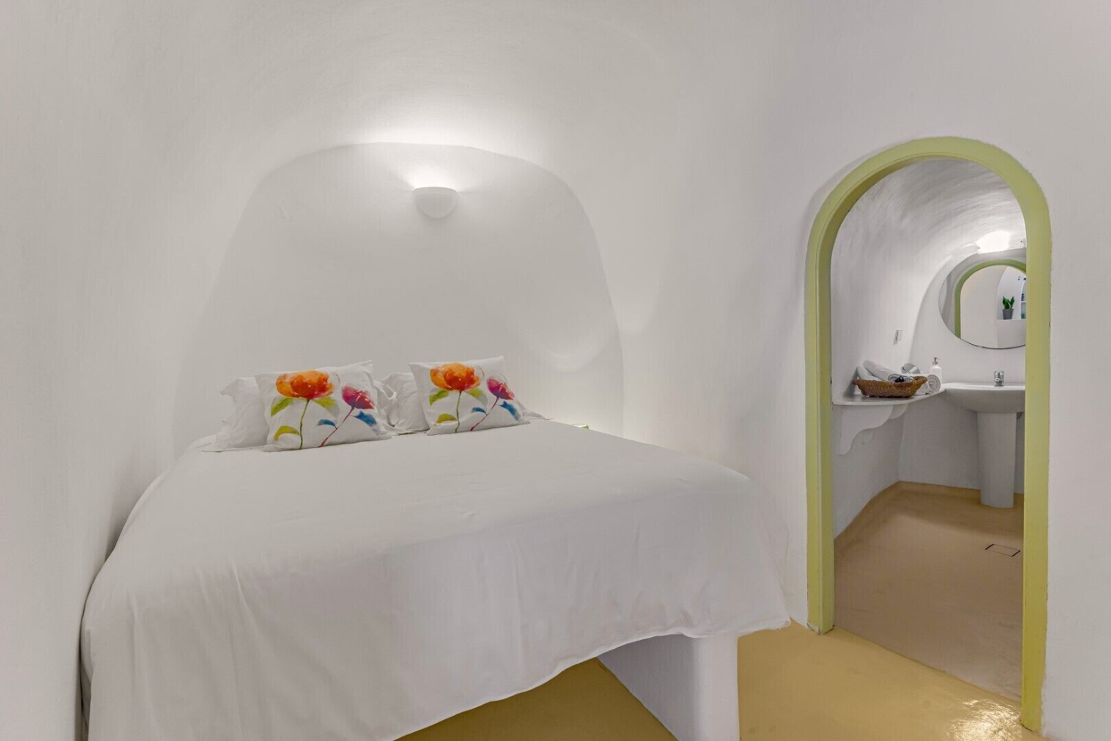 A minimalist bedroom with a white bed, colorful pillows, and a green archway leading to a bathroom.