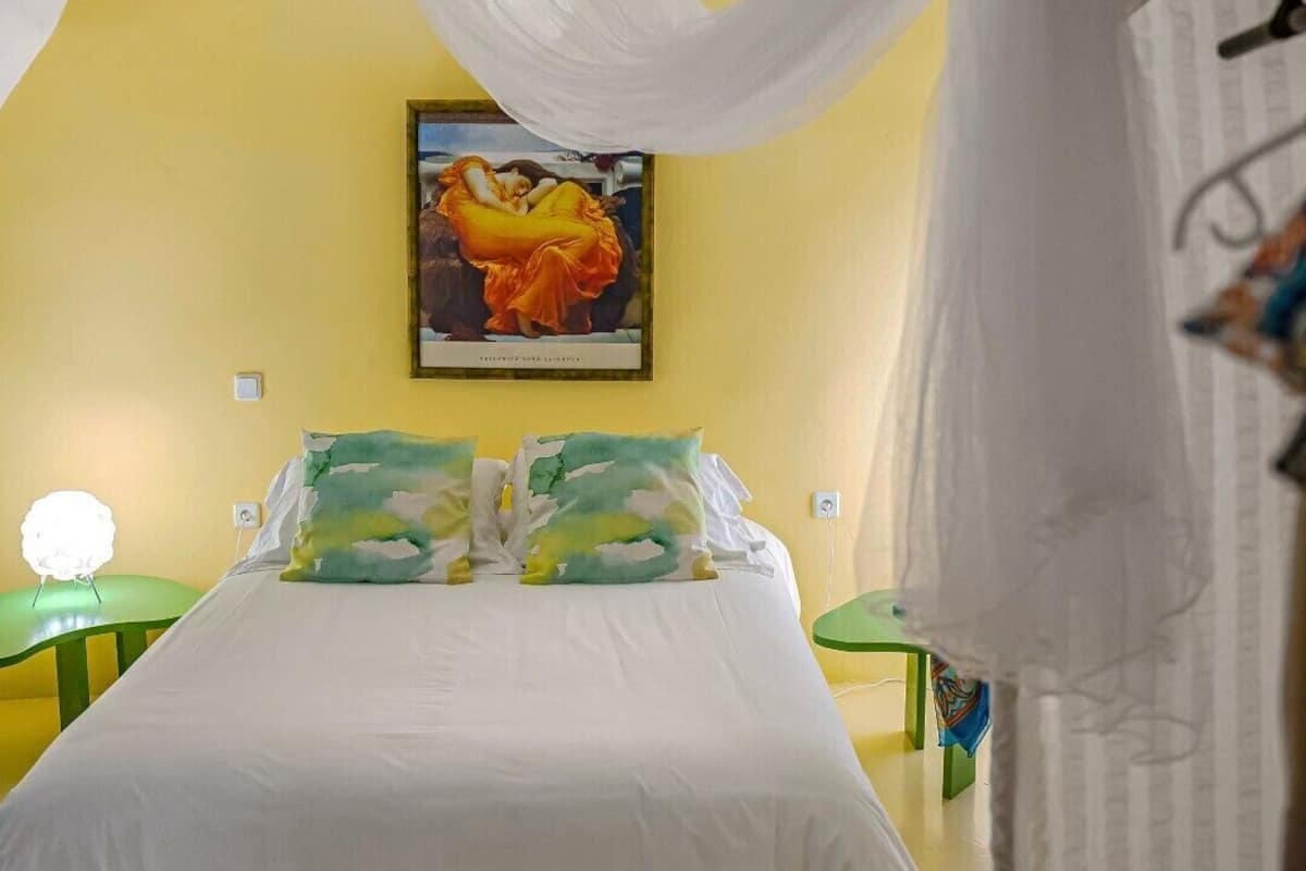A bedroom with a bed, a painting on the wall, and a hanging canopy.