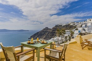 A table set with breakfast items overlooking a coastal view with white buildings and a cliff. - Sensyo Caves (Santorini)