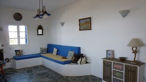 A room with a blue sofa, a stone floor, a cabinet with decorative items, and a window with curtains. - Villa with sea view, Antiparos, Greece (Agios Georgios)