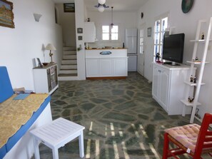 Una cocina compacta con armarios blancos, un refrigerador, un microondas y un televisor en una estantería.