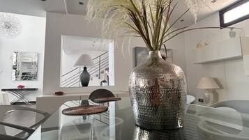 Un comedor moderno con una mesa de vidrio, una silla tejida y un jarrón decorativo con plumas de pluma.