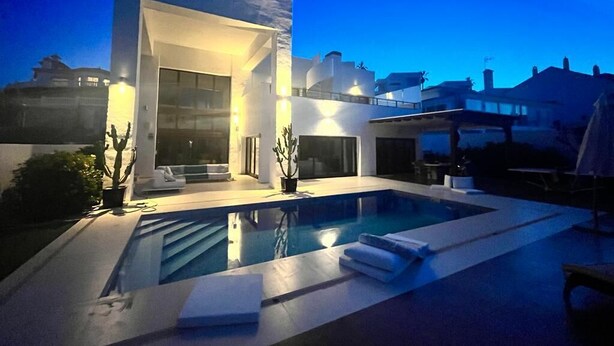 Uma casa moderna de dois andares com piscina, janelas amplas e área de estar externa.