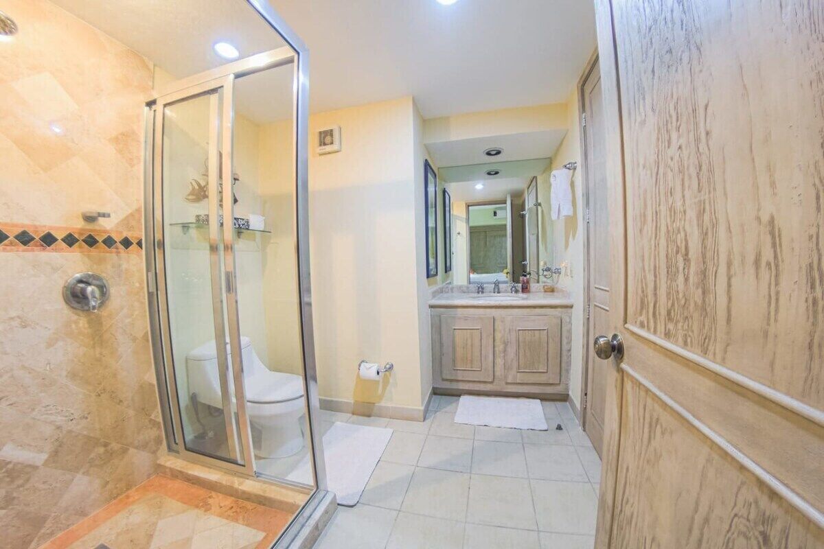 A bathroom with a glass shower enclosure, a toilet, a sink with a mirror, and wooden cabinets.