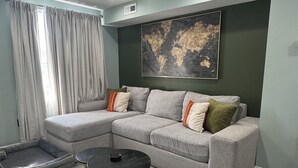 Een moderne woonkamer met een hoekbank, een ronde salontafel en een groot abstract schilderij aan de muur.
