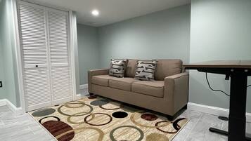 A room with a beige sofa, patterned rug, and a table with a black base.